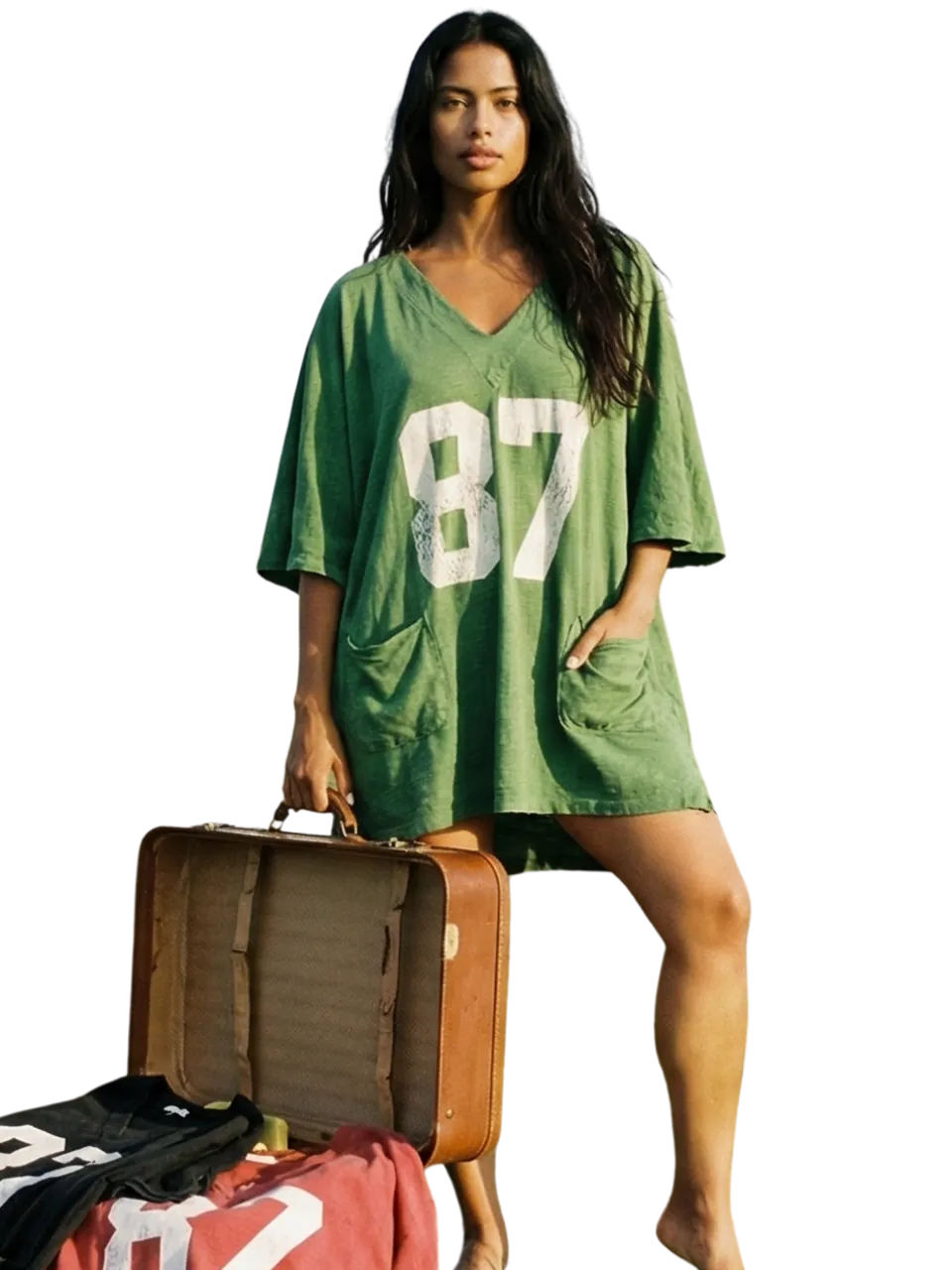 Model in an oversized green jersey standing beside stacked vintage luggage
